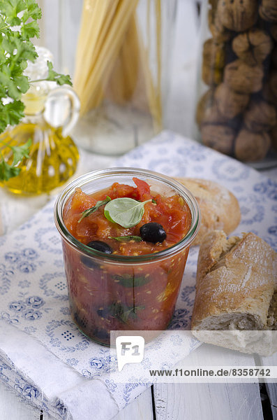 Geleeglas mit Tomatensauce  schwarzen Oliven und Basilikumblättern  serviert mit Weißbrot  Studioaufnahme