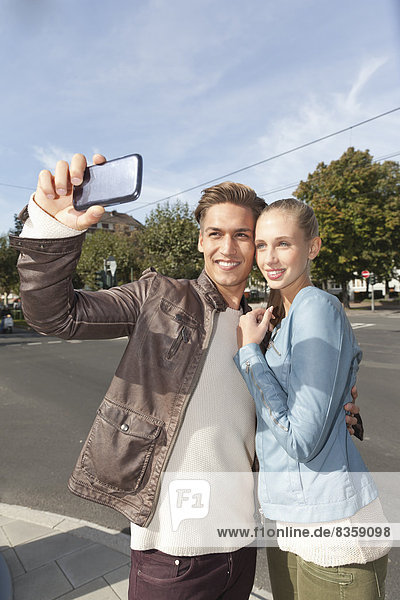 Ein junges Paar fotografiert sich mit einem Smartphone.