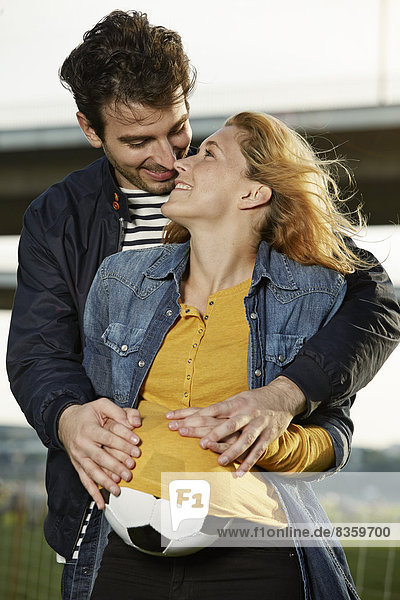 Young couple embracing  woman hiding ball under shirt