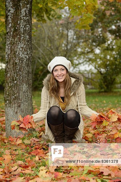 Lächelnde junge Frau an einem Baum im Herbst