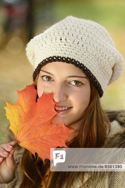 Smiling young woman holding autumn leaf  portrait