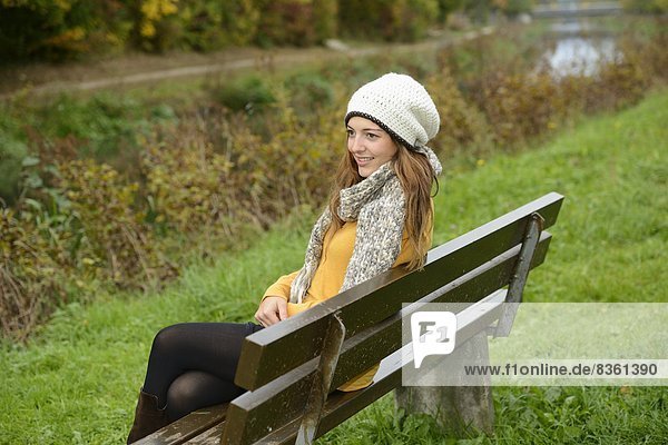 Lächelnde junge Frau sitzt auf einer Bank im Herbst