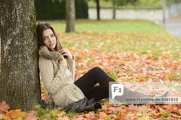 Junge Frau sitzt unter einem Baum im Herbst