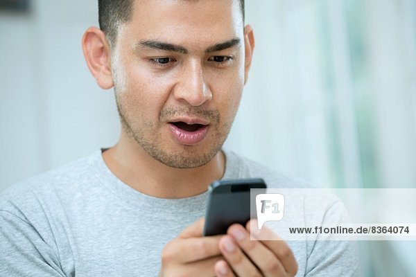 Mittlerer Erwachsener Mann schaut überrascht auf Smartphone