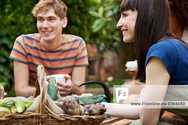 Freunde sitzend im Garten mit Korb mit frischem Gemüse