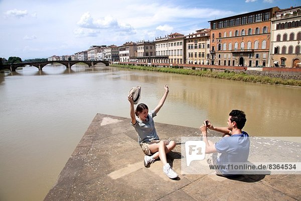 Mann fotografiert Frau mit Ponte alle Grazie im Hintergrund  Florenz  Toskana  Italien