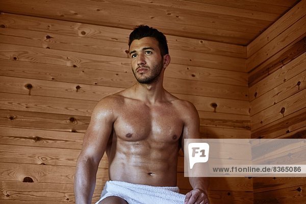 Junger muskulöser Mann sitzt in der Sauna