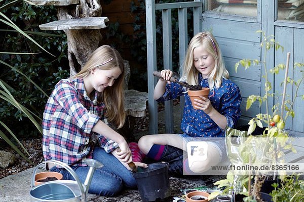 Two girls in garden planting seeds into pots
