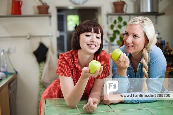Zwei junge Frauen in der Küche halten Äpfel.