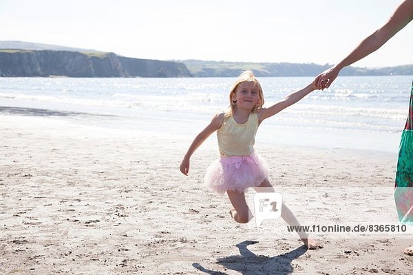 Mother and daughter wearing tutu running on beach  Wales  UK