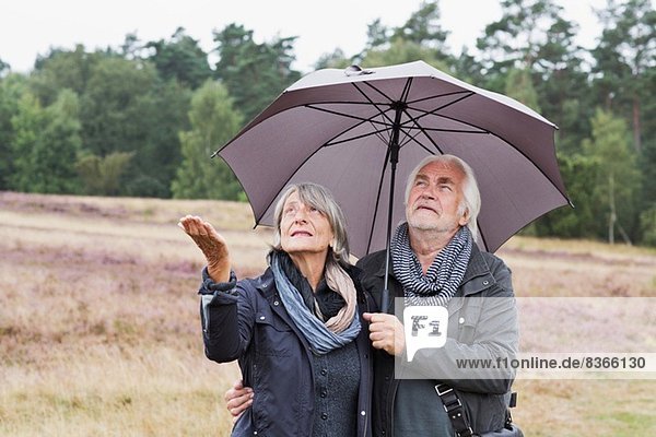 Seniorenpaar unter dem Schirm auf Regen prüfen