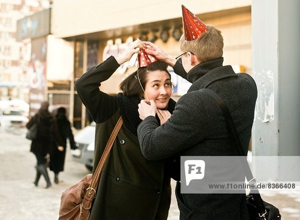 Junges Paar auf der Stadtstraße  das Partyhüte anpasst.
