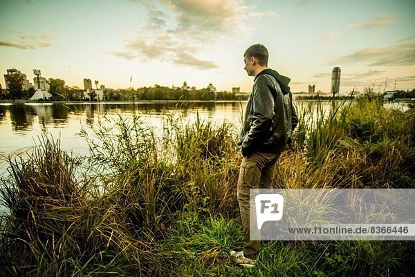 Junger Mann auf Gras stehend mit Blick auf das Wasser  Russland