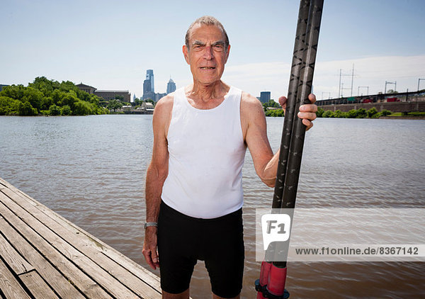 Senior man on pier holding oars