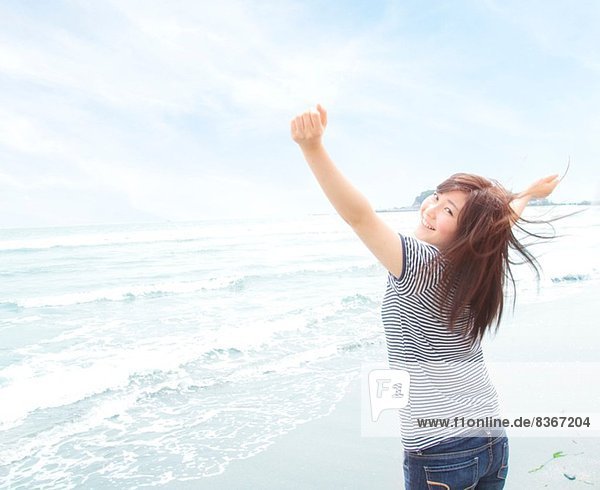 Portrait of young woman on beach with arms raised  looking over shoulder