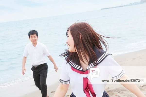 Junges Paar in Schuluniform läuft am Sandstrand
