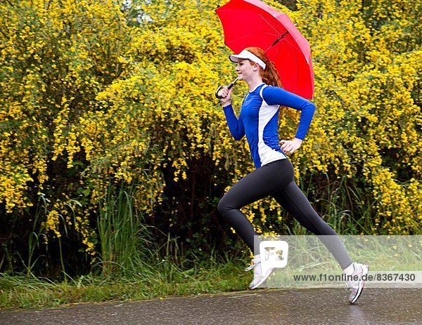 Teenage girl jogging with umbrella on road  Bainbridge Island  Washington  USA