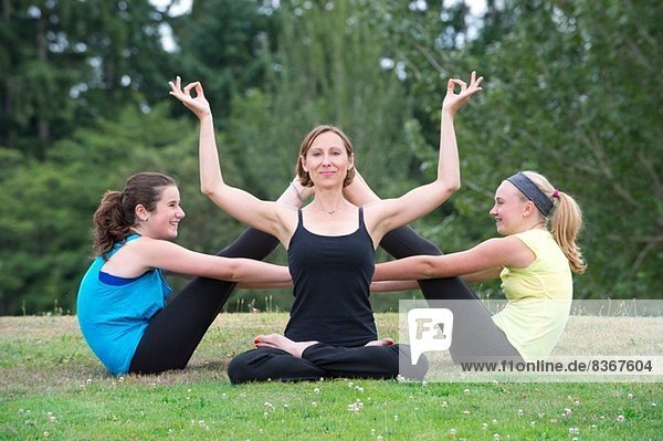 Teenagermädchen und Yogalehrer auf Rasen sitzend