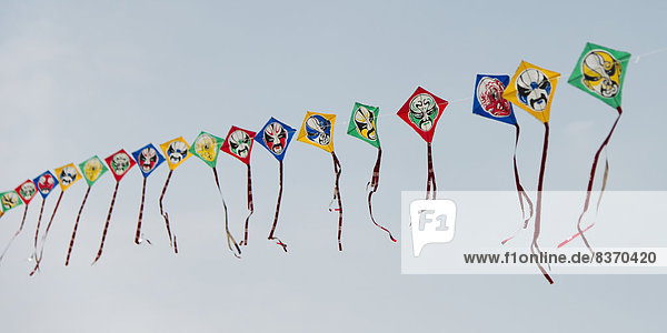 Colourful Kites With Faces On Them In A Row Against A Blue Sky