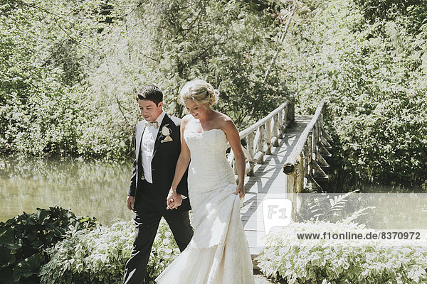 A Bride And Groom Walk Hand In Hand With A Bridge Going Over A Creek Pemberton  British Columbia  Canada
