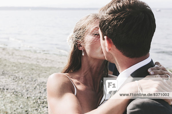 A Bride And Groom Kissing On A Beach At The Water's Edge Kirkland  Washington  United States Of America