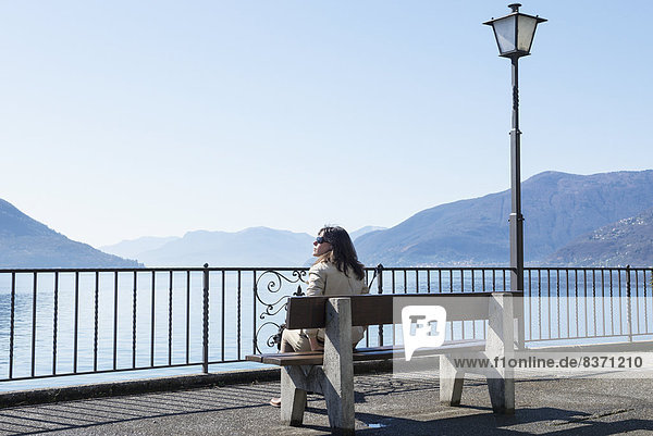 A Woman Sitting On A Bench Overlooking Lake Maggiore Brissago  Ticino  Switzerland