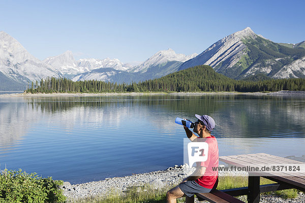 A Man Drinks From A Water Bottle On The Edge Of A Lake Overlooking The Rocky Mountains Kananaskis  Alberta  Canada
