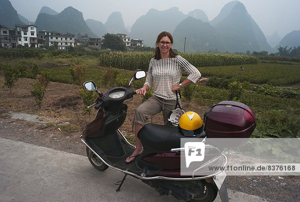 A Woman Poses With Her Motor Scooter With The Peaked Mountains In The Background  Yangshuo  China