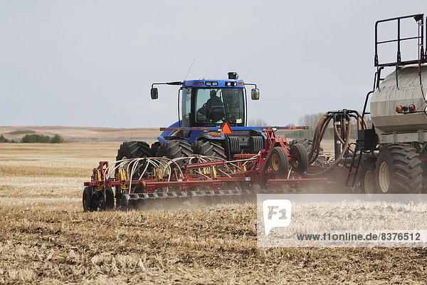 Close Up Of An Air Seeder In A Field With A Tractor And Blue Sky In The Background  Acme  Alberta  Canada