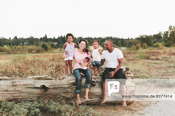 Interracial Family Sitting On Log On Beach  British Columbia  Canada
