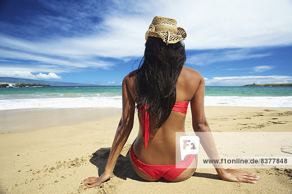 A young woman in a red bikini sitting on the beach of an hawaiian island Maui  Hawaii  United States of America