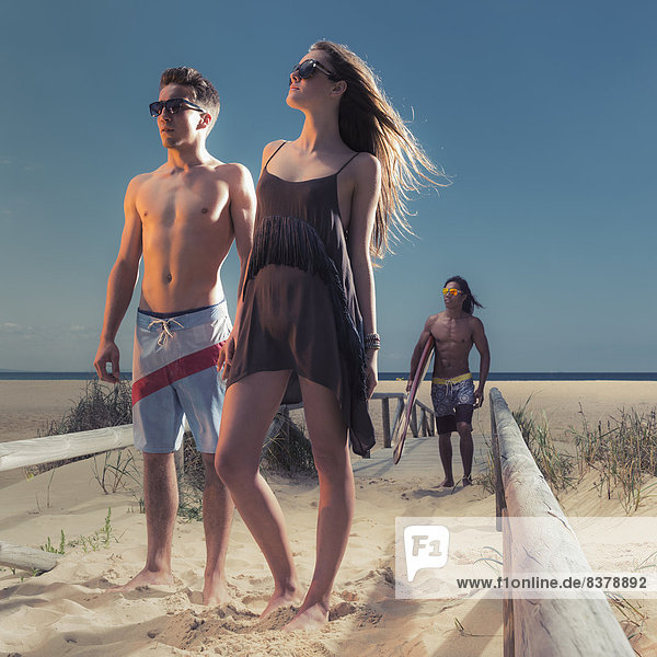 Young Man And Woman In Swimwear On A Sandy Beach With A Surfer Carrying A Surfboard Tarifa  Cadiz  Andalusia  Spain