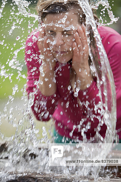 Junge Frau spritzt sich Wasser ins Gesicht