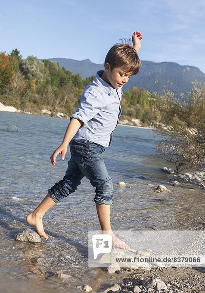Kleiner Junge läuft barfuß in einem Fluß