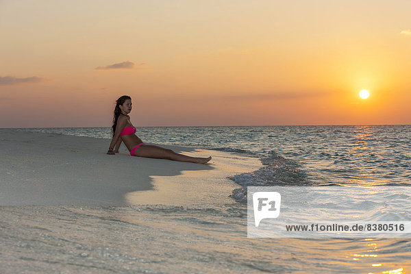 Frau sitzt am Strand bei Sonnenuntergang  Indischer Ozean  Malediven