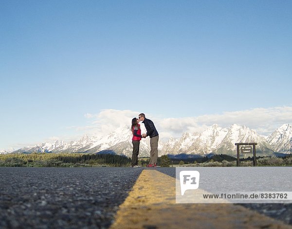A young couple kisses with mountains in the background