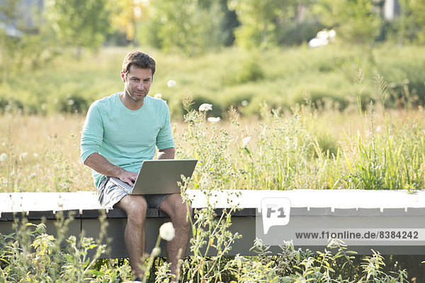 Mann  der den Laptop benutzt  während er in der Natur sitzt.