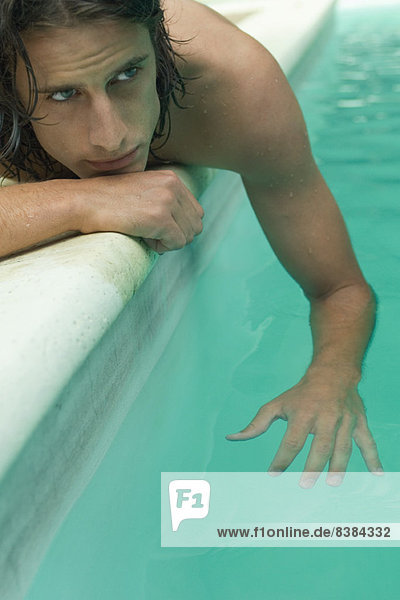 Junger Mann neben dem Schwimmbad liegend  baumelnder Arm im Wasser
