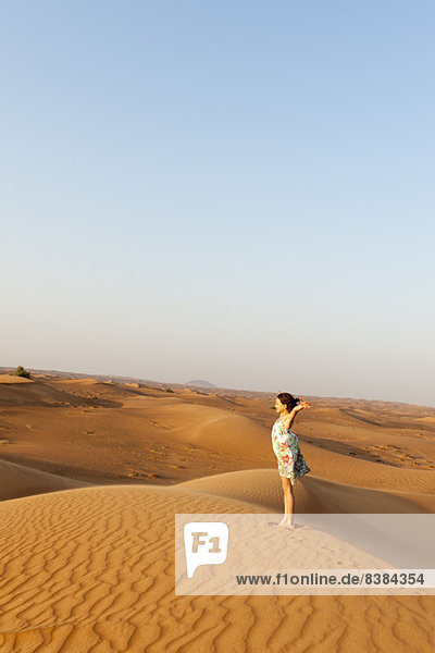 Girl standing in desert with arms raised in air