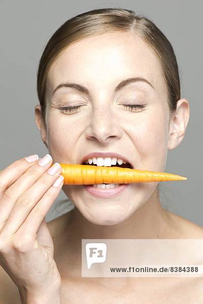 Young woman biting into carrot  eyes closed