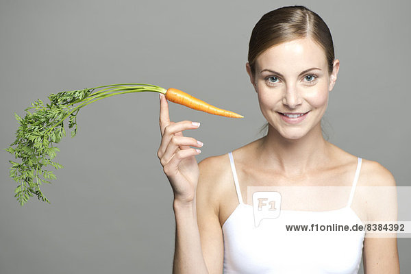 Young woman balancing carrot on fingertip
