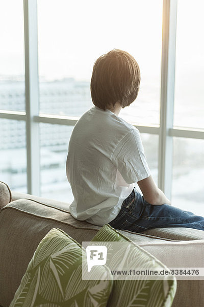 Teenager-Junge sitzt auf dem Sofa,  schaut aus dem Fenster,  Rückansicht