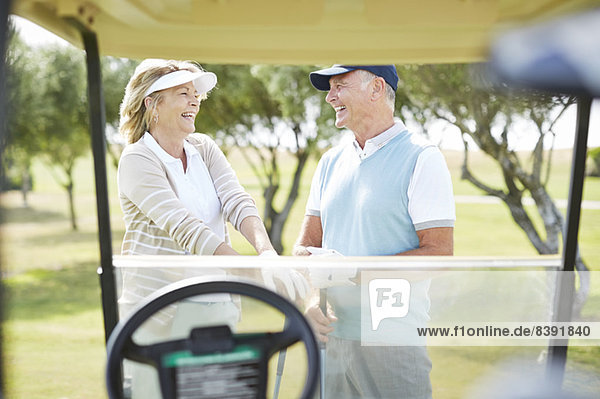 Seniorenpaar lacht auf dem Golfplatz