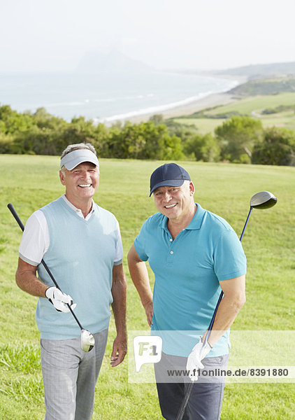 Senioren lächeln auf dem Golfplatz mit Blick auf den Ozean