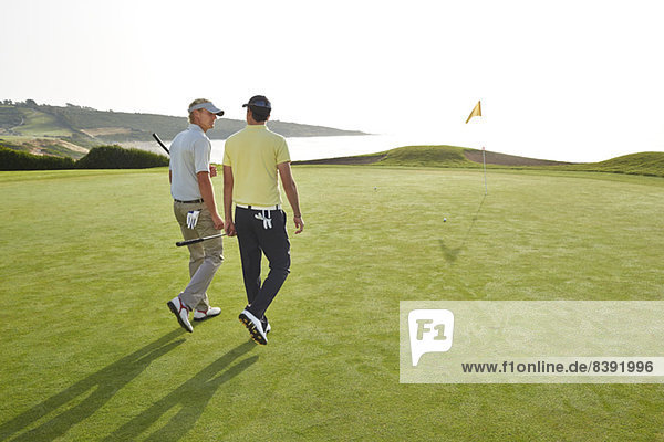 Männer  die zum Loch auf dem Golfplatz mit Blick auf den Ozean gehen.