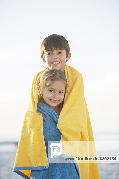 Bruder und Schwester in Handtücher gewickelt am Strand