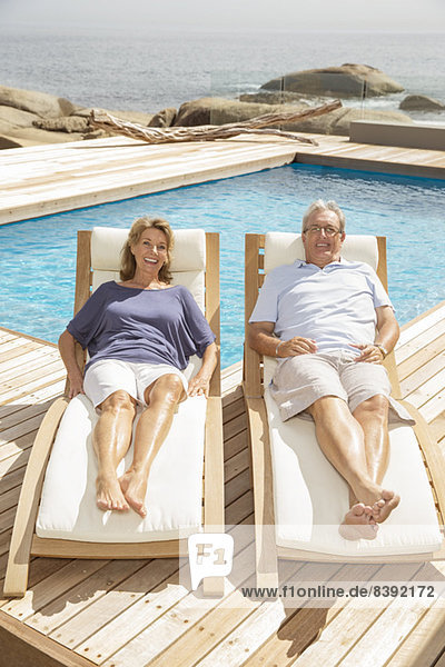 Seniorenpaar auf Liegestühlen am Pool liegend