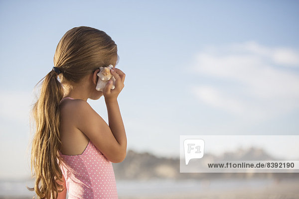 Mädchen hört Muschel am Strand