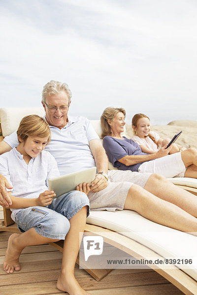 Grandparents and grandchildren using digital tablets at poolside