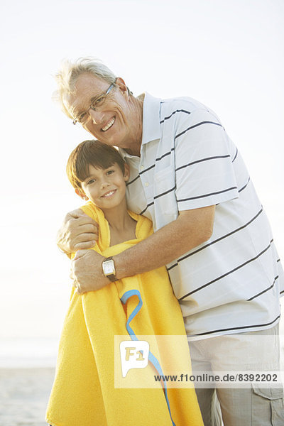 Großvater umarmt Enkel am Strand